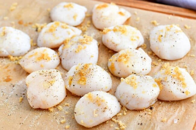 Uncooked scallops are seasoned and placed on a piece of parchment paper.