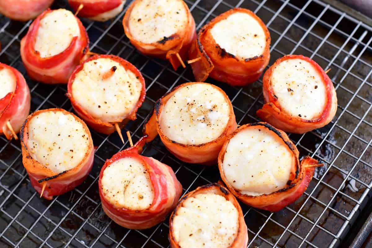 Cooked bacon wrapped scallops are on a wire rack. 