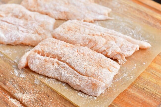 Uncooked cod is coated in flour and placed on a sheet of parchment paper. 