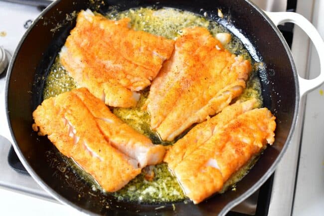 Filets are being cooked in a buttery sauce in the skillet.