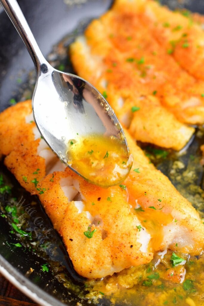 Butter sauce is being drizzled over a fillet with a spoon.