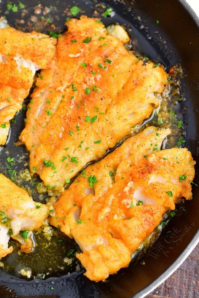 Several cod fillets are in a large black skillet. 