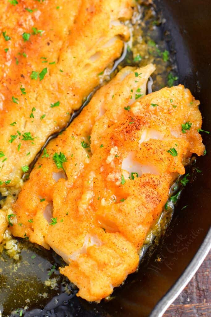 Cod fillets are fully cooked in a large black skillet.