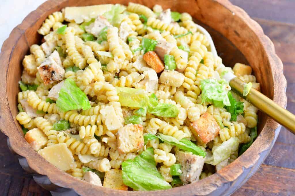 The tossed pasta salad is presented in a large wooden bowl. 