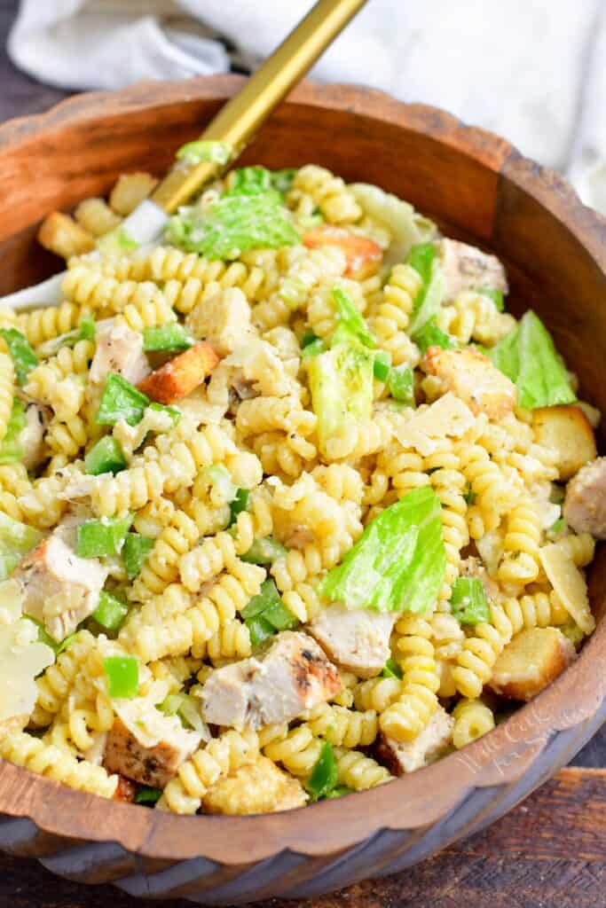Chicken caesar pasta salad is in a large wooden bowl. 