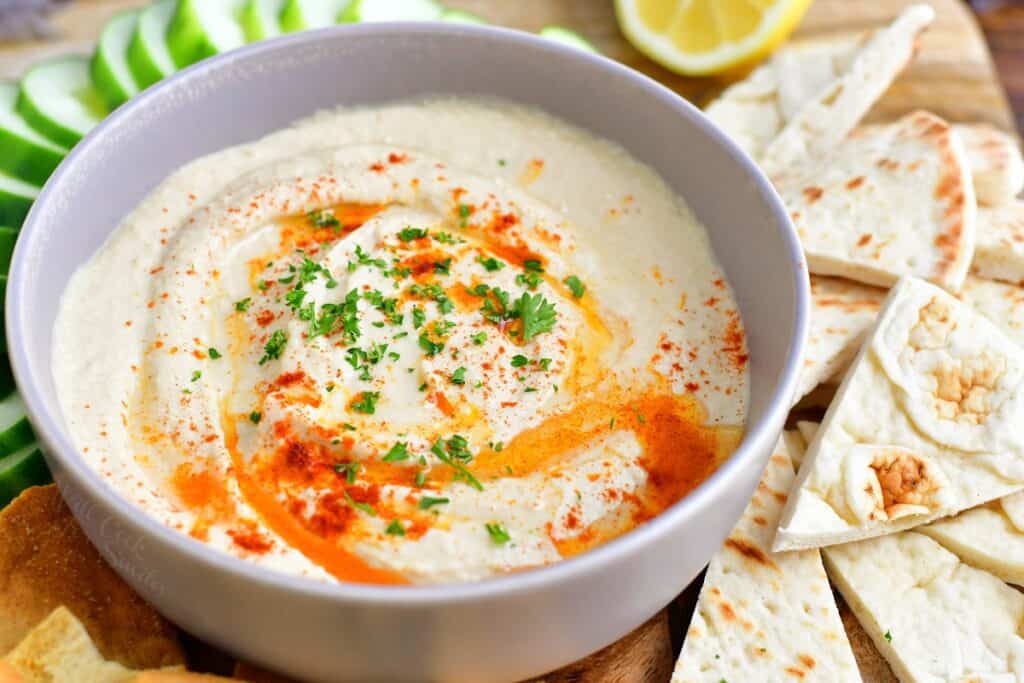 Hummus is in a white bowl and garnished with paprika and olive oil.