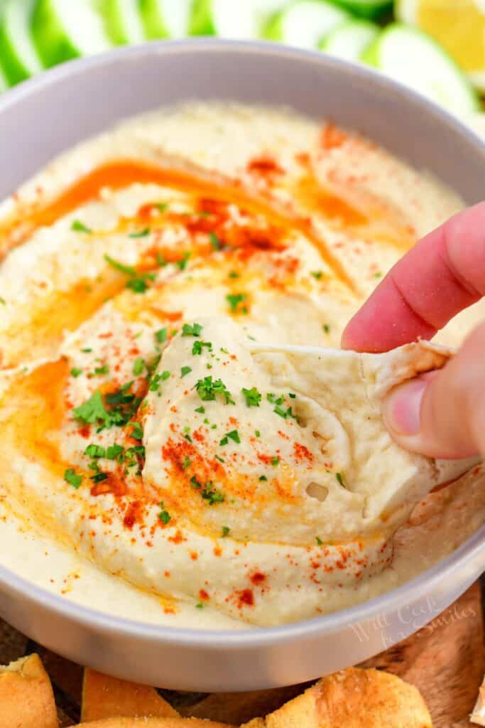 A piece of naan is being dipped into hummus.