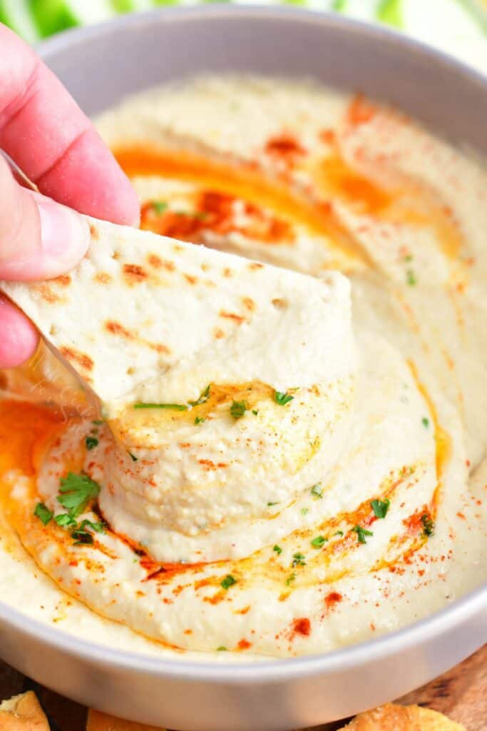 A piece of naan is being dipped into hummus.