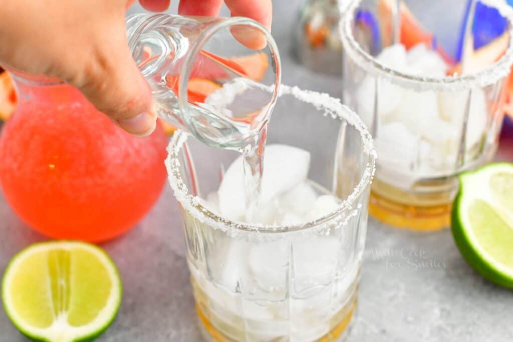 A shot of tequila blanco is being poured into a rimmed glass.