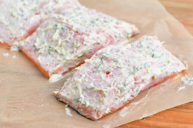 Salmond filets are covered with a fresh mayonnaise mixture on a prepared baking sheet.