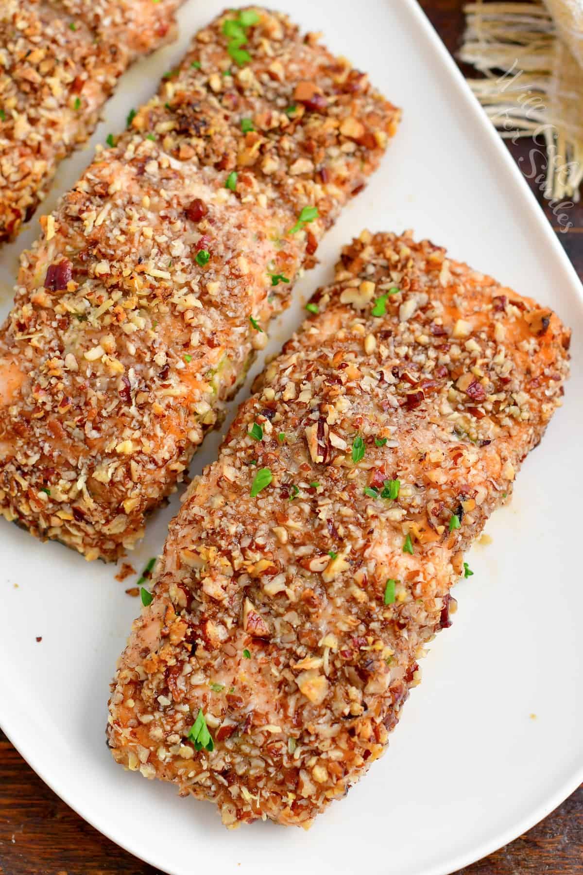 Three baked salmon filets are on a white plate.