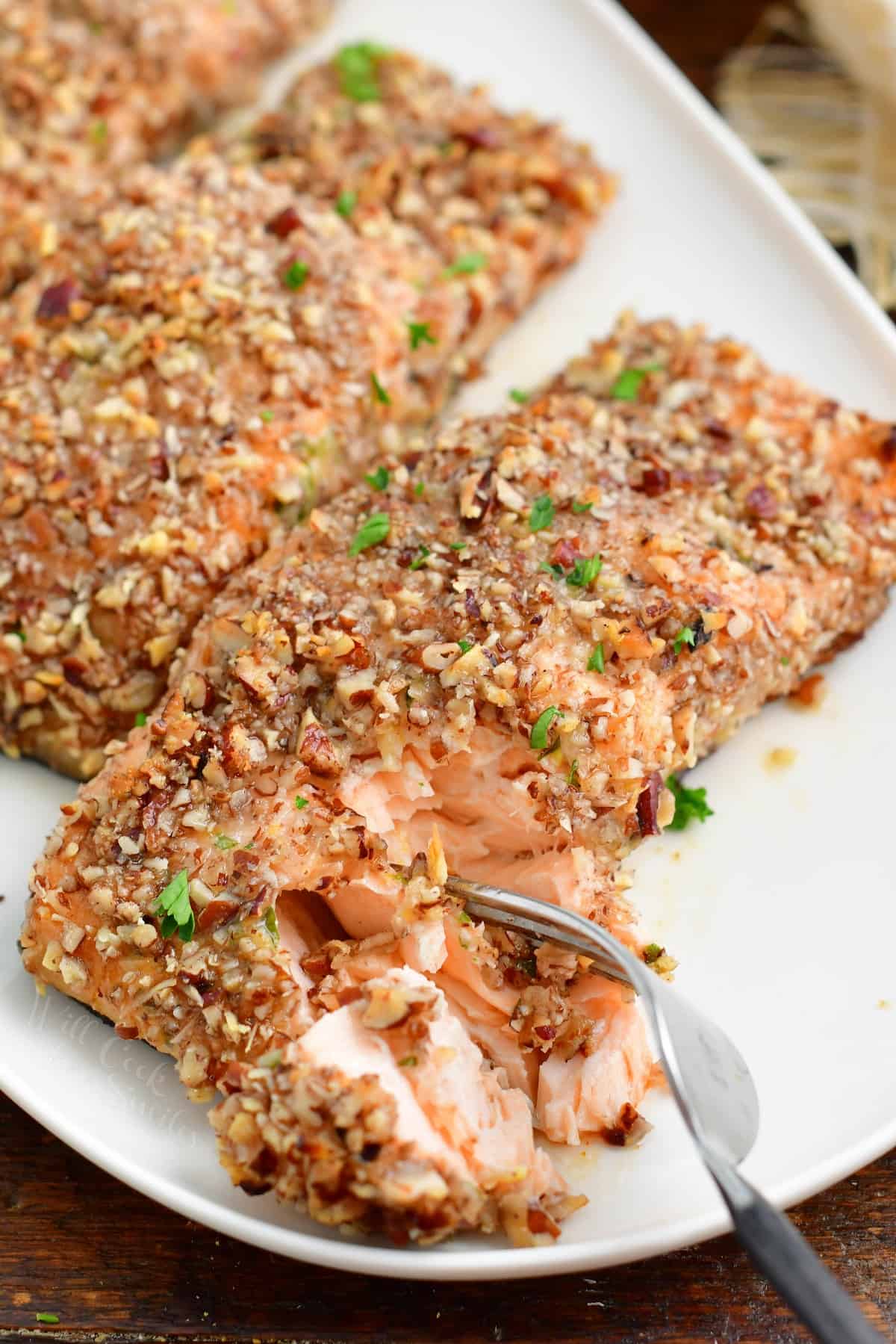 A fork is removing bite sized piece of salmon from the white plate.