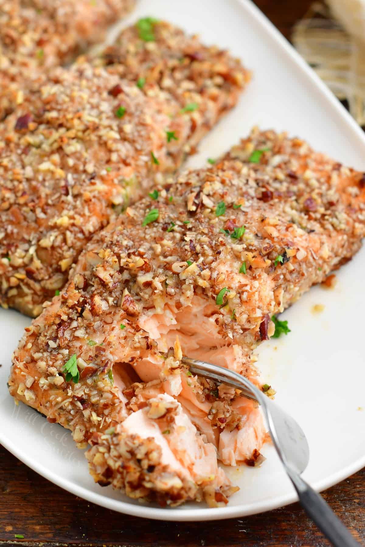 A fork is removing bite sized piece of salmon from the white plate. 