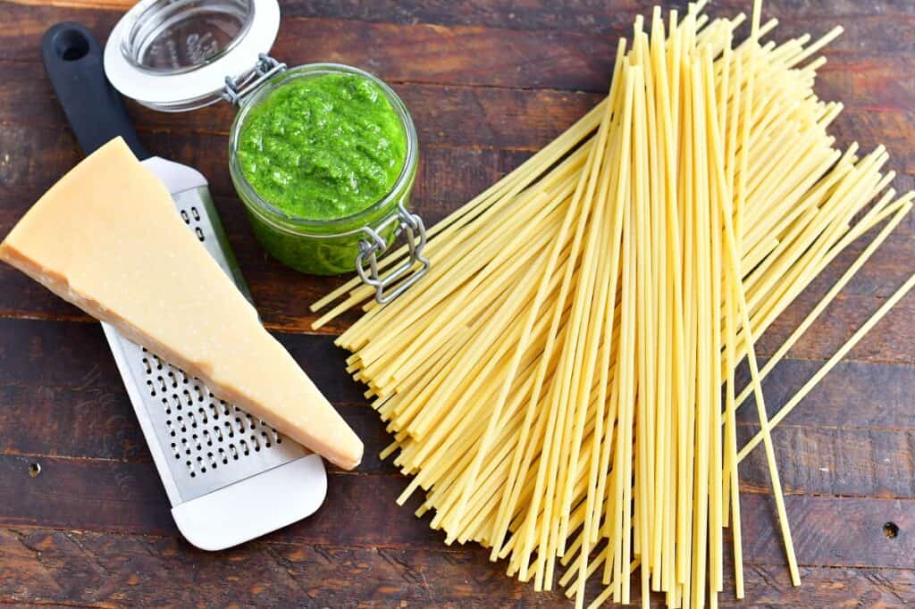 The ingredients for pesto pasta are placed on a wooden surface.