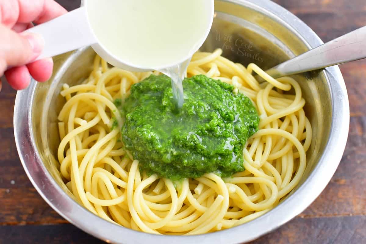 Noodles in a large bowl are topped with fresh pesto and cooking water.