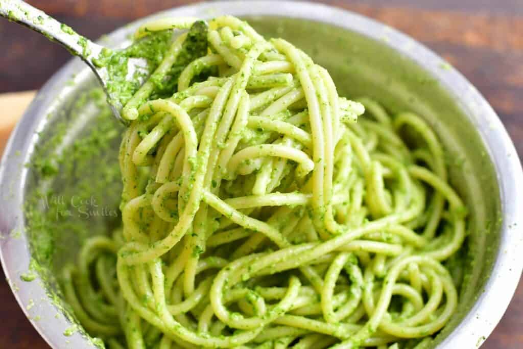 Pasta is being tossed with pesto sauce and pasta water.
