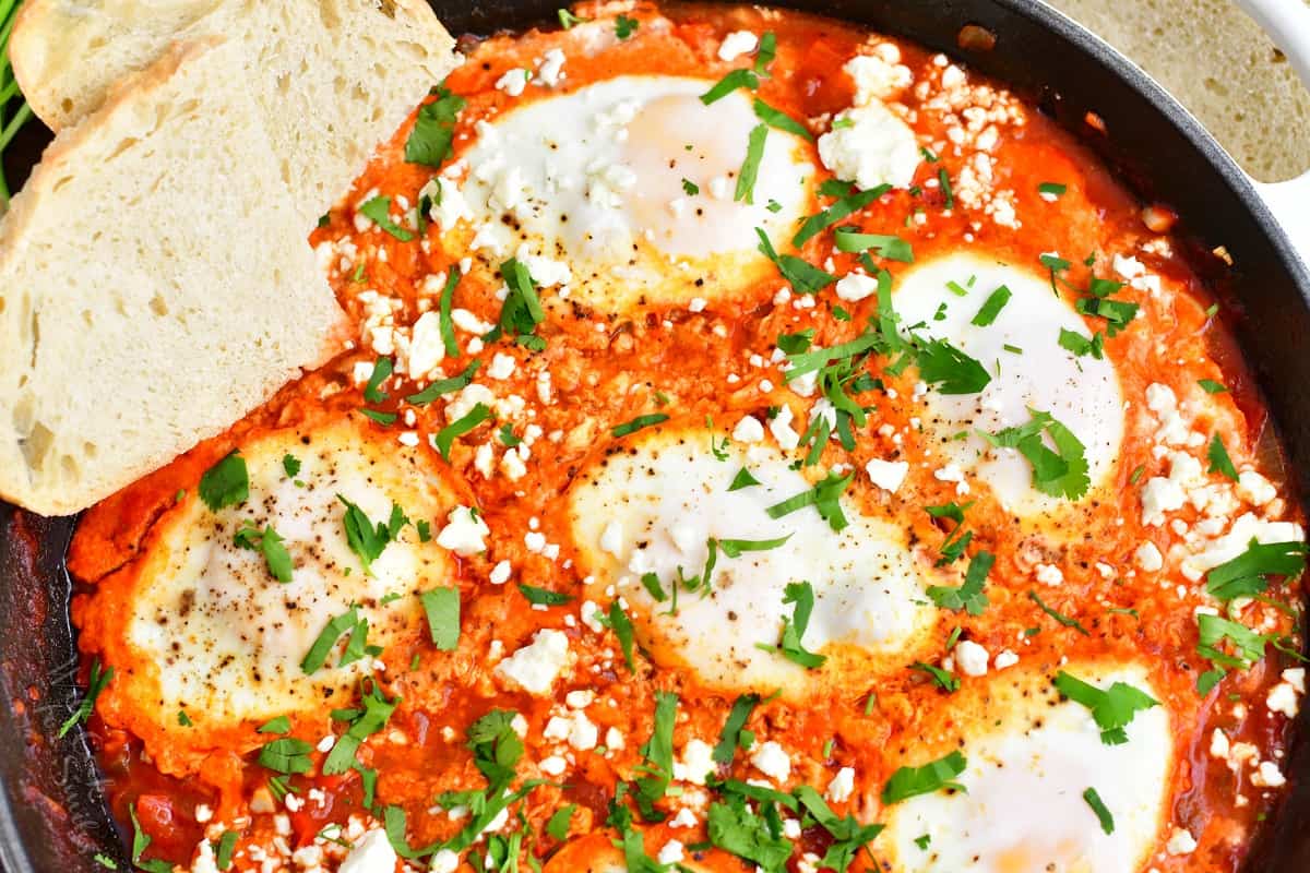 Eggs are fully cooked in the middle of tomato stew and garnished with fresh greens. 