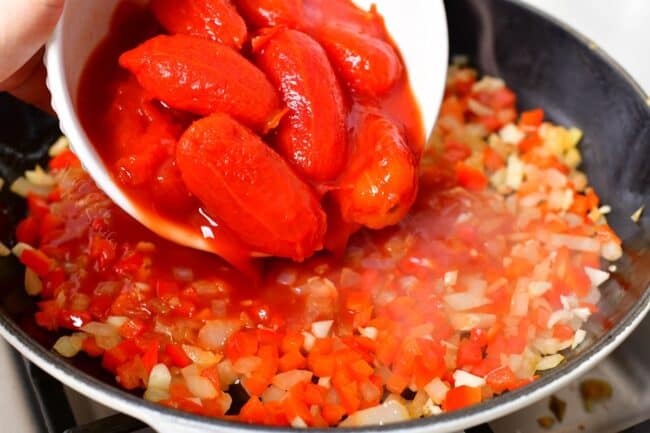 Tomatoes are being added to the skillet.