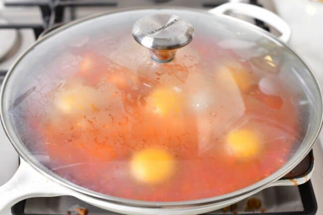 A skillet has been covered, showing raw eggs and tomato stew cooking inside.