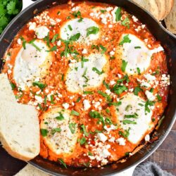 A few slices of bread are placed next to a black skillet filled with shakshuka.