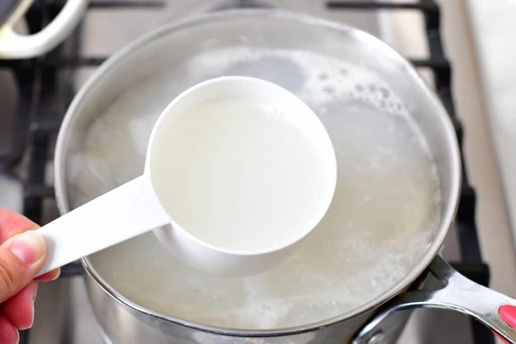 A cup of boiling water is being reserved in a white measuring cup.