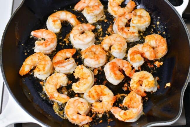 Shrimp is cooking in a large black skillet.