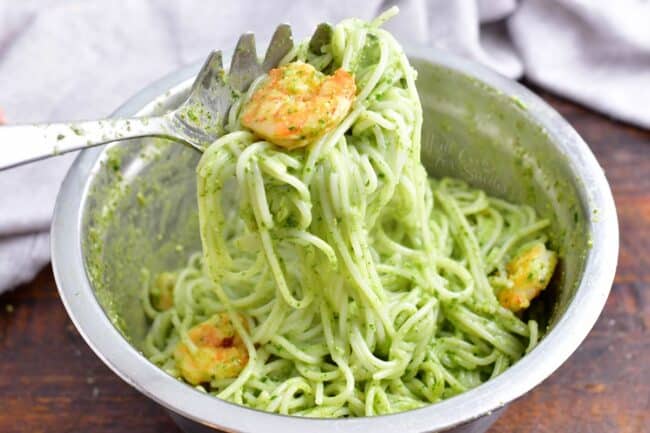 A large serving spoon is lifting noodles and shrimp from a bowl. 