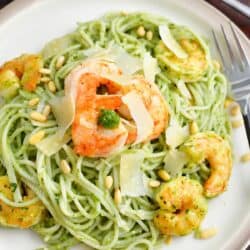 A white plate is filled with pesto pasta and shrimp.