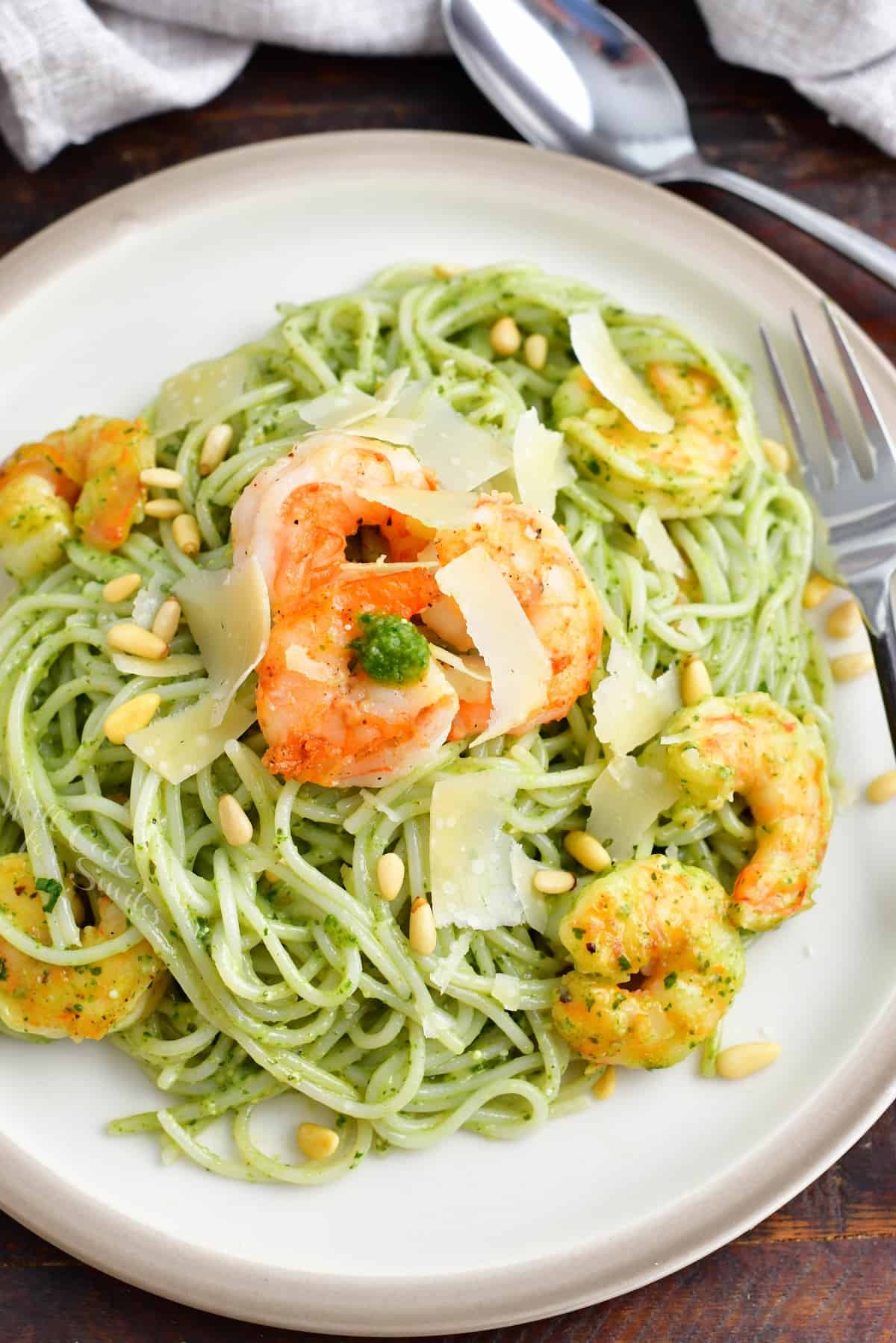 A white plate is filled with pesto pasta and shrimp. 