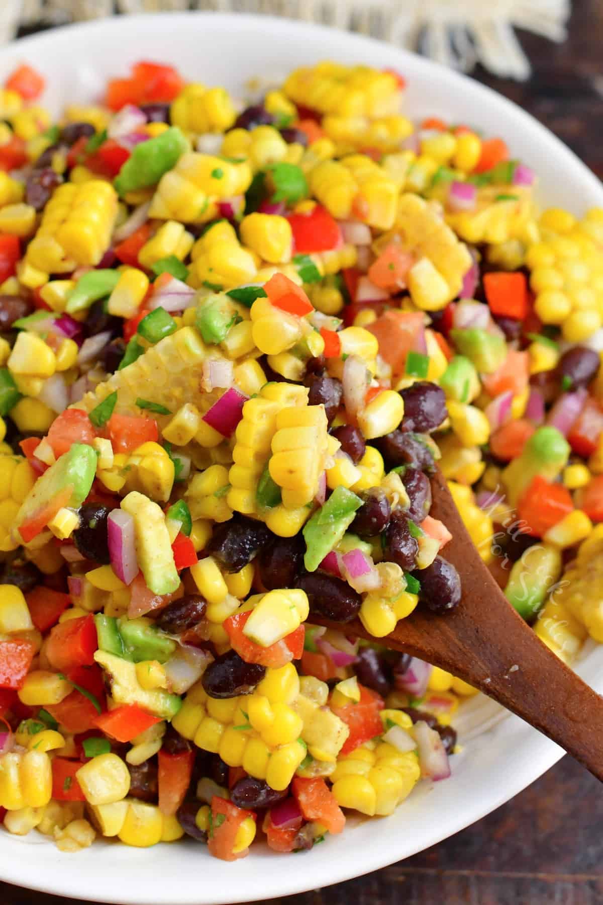 The salad is being lifted from the bowl with a wooden spoon. 