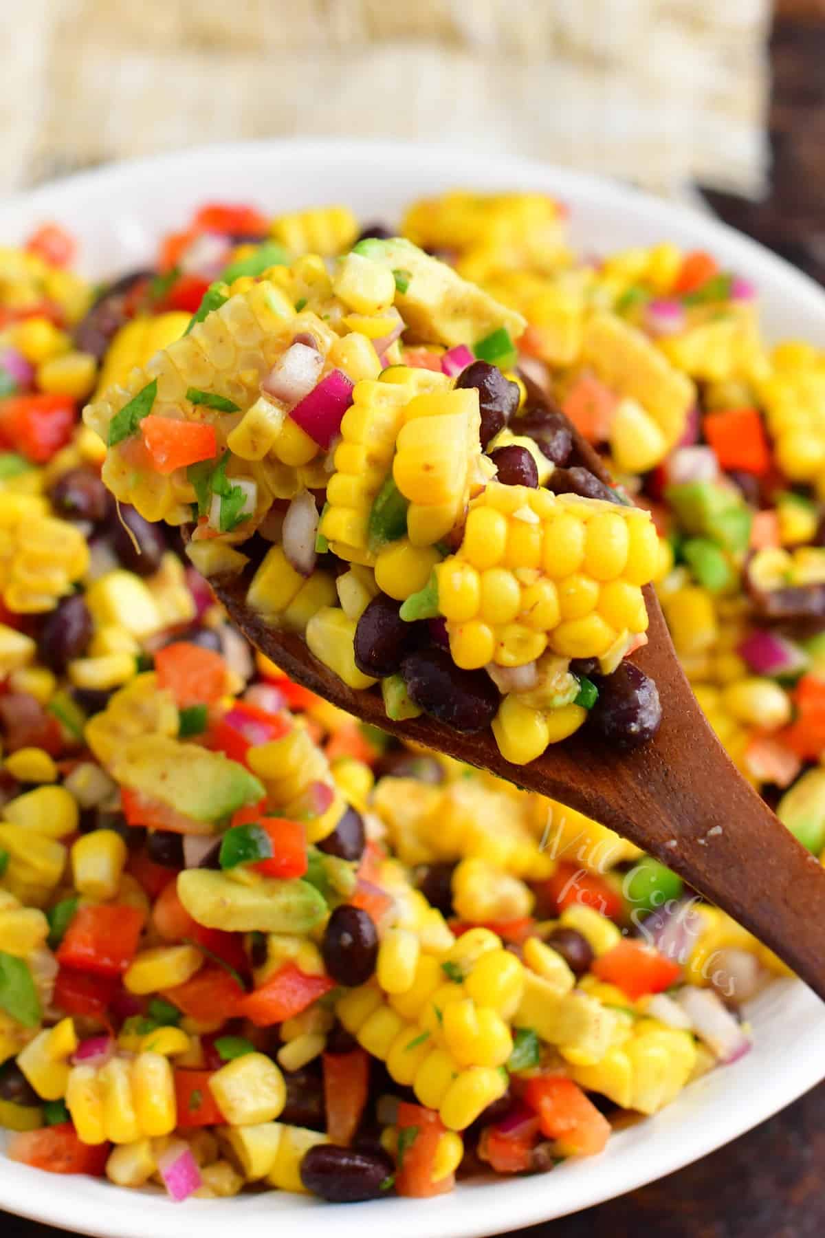 A wooden spoon is scooping a serving of salad from a large white bowl. 