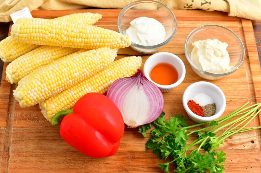 The ingredients for creamy corn salad are placed on a wooden cutting board. 