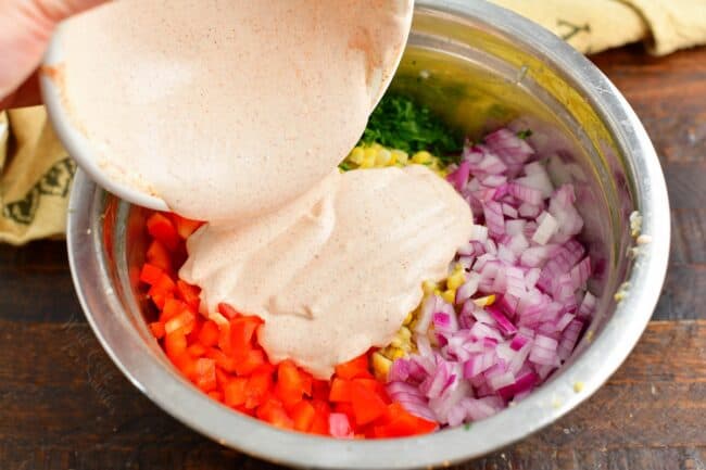 The creamy mixture is being poured over the ingredients in a large bowl.