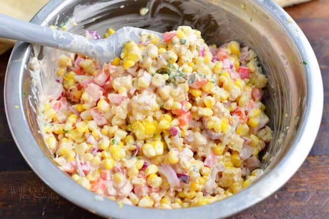 Corn salad is being mixed in a metal bowl. 