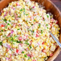 A large wooden serving bowl is filled with freshly made corn salad.