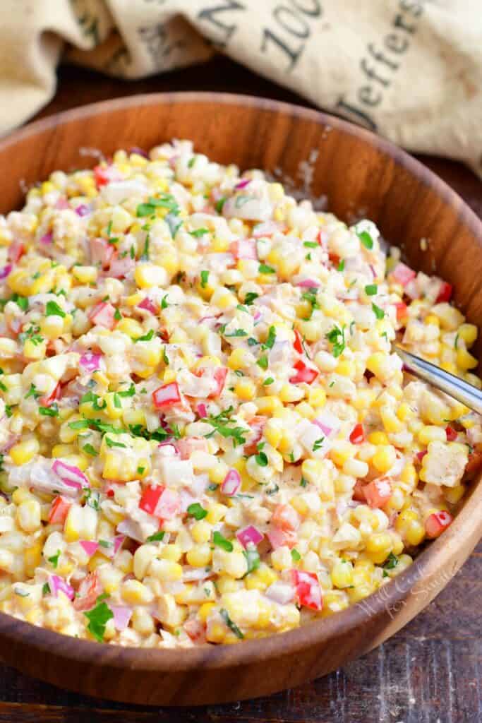 A wooden bowl is filled with creamy corn salad.