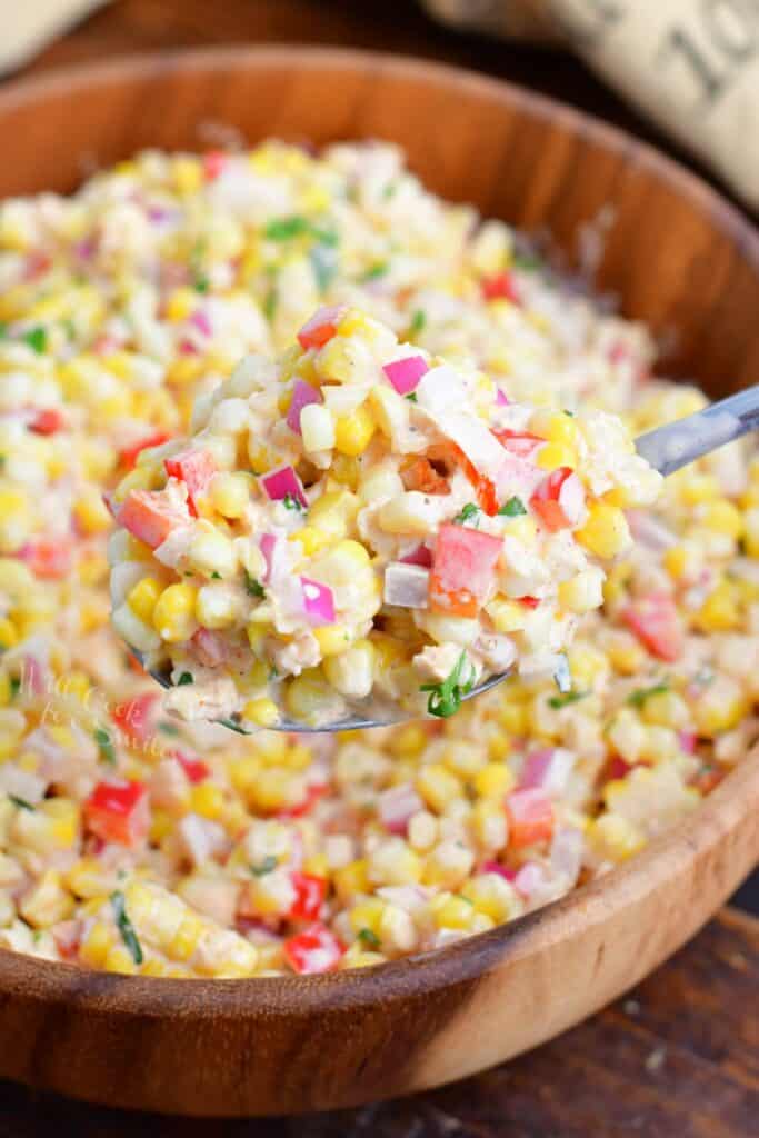 A spoonful of corn salad is being lifted from the large bowl. 