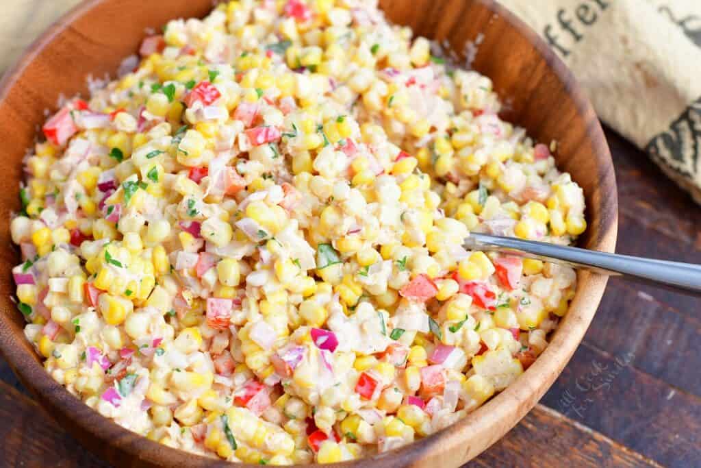 A serving spoon has been placed in the creamy corn salad. 