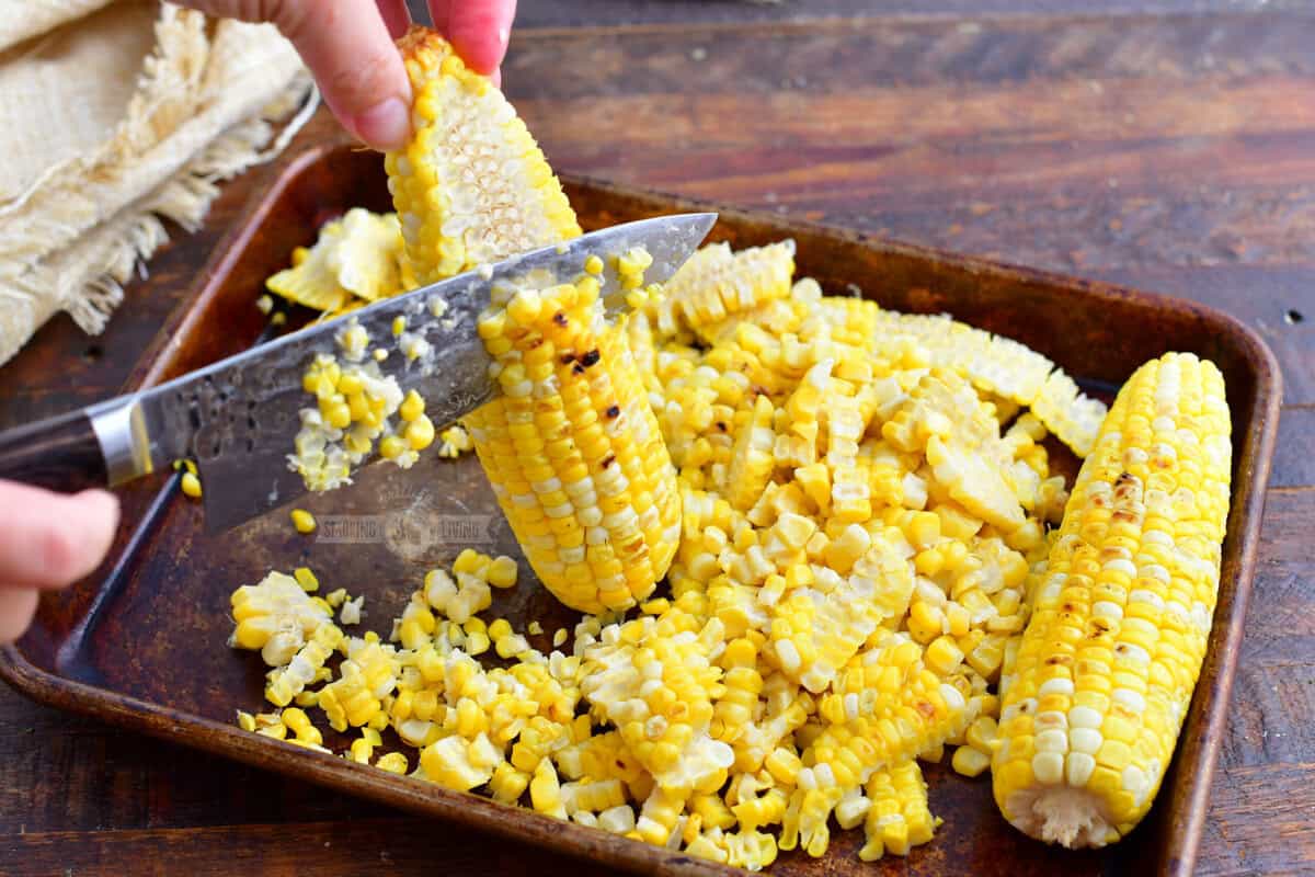 cutting the corn off the cob on a metal baking sheet.