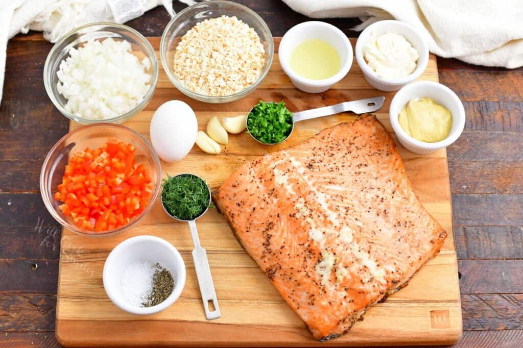 Ingredients for salmon burgers are on a wooden cutting board. 