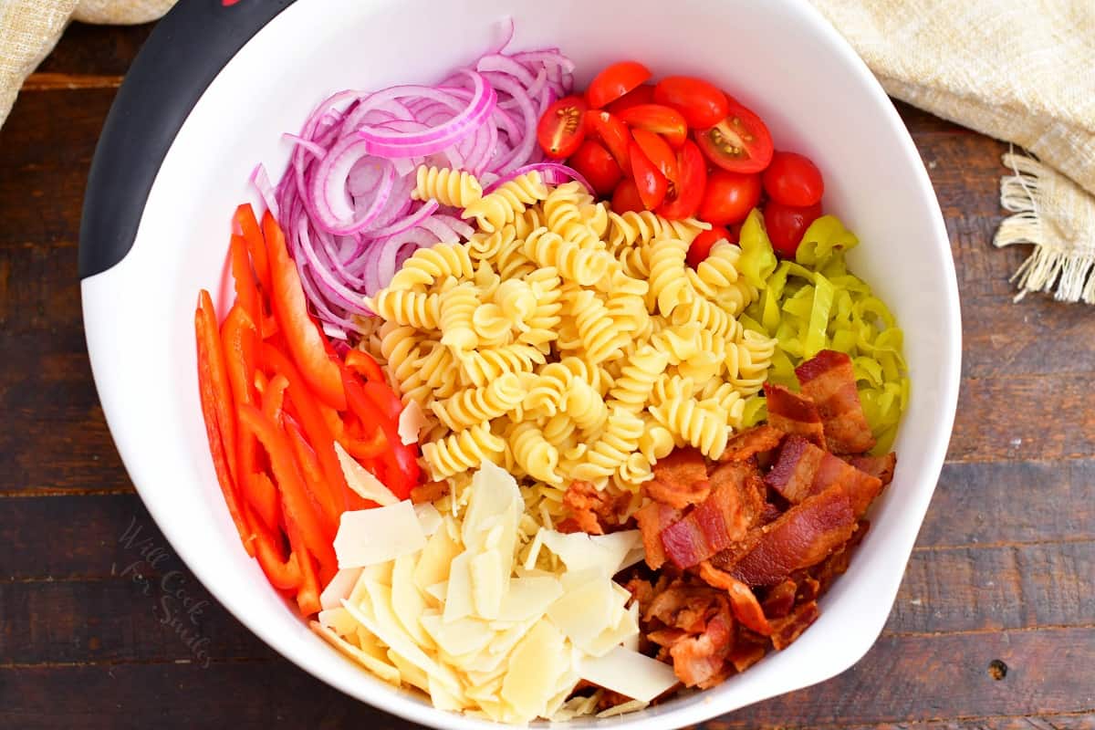 All of the ingredients for pasta salad are in a large white mixing bowl. 