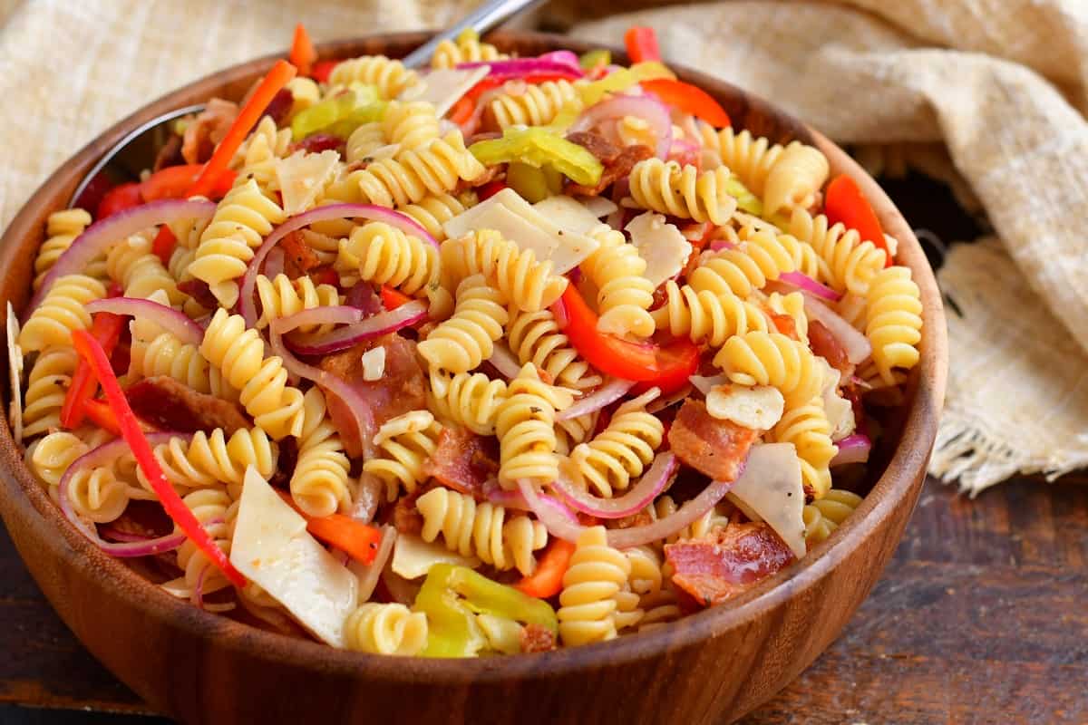 A pasta salad is presented in a large wooden bowl, ready to be served. 