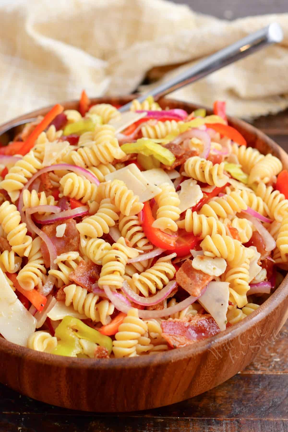 A tea cloth is pictured behind a bowl filled with pasta salad.