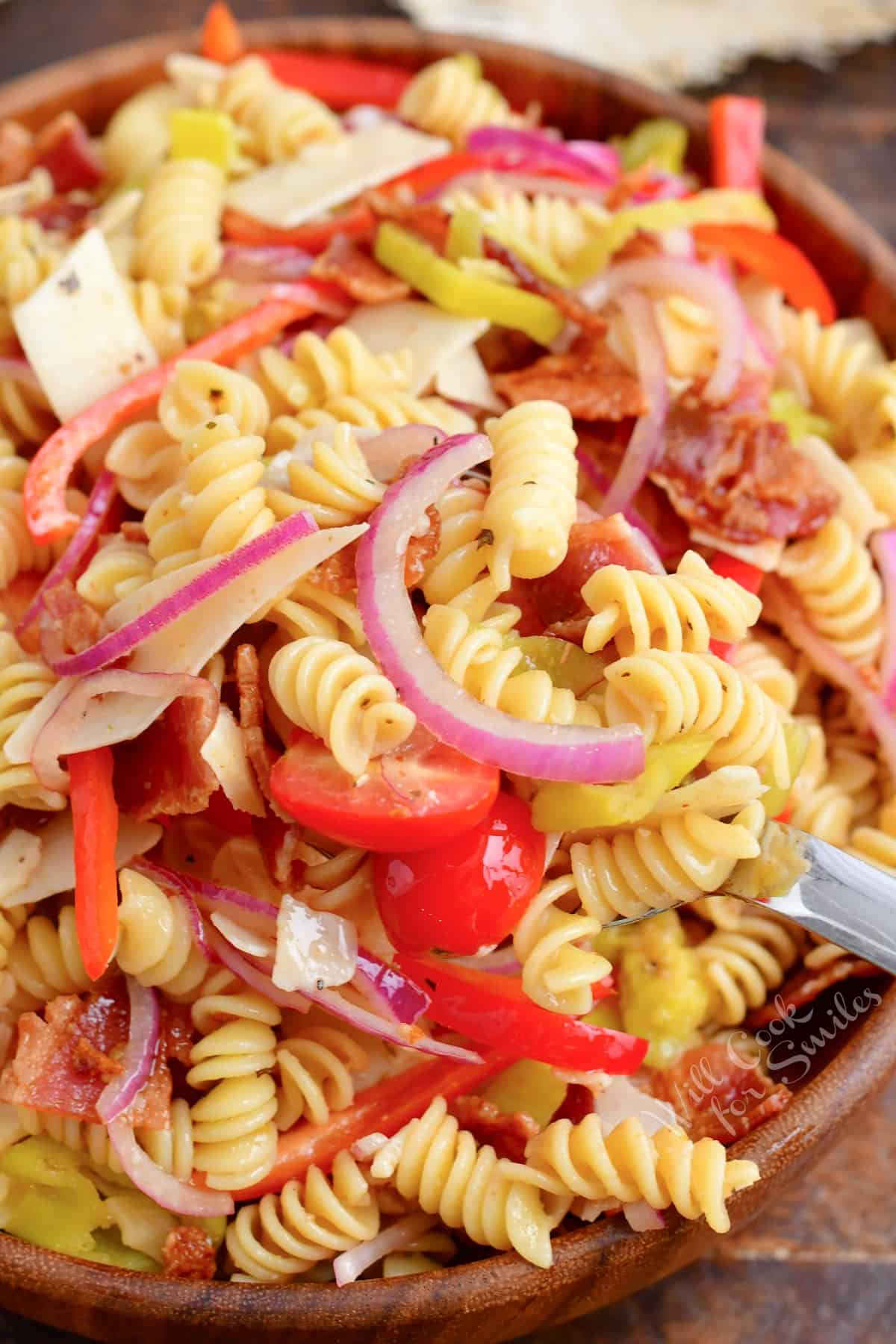 Pasta salad is tossed and presented in a large wooden bowl. 