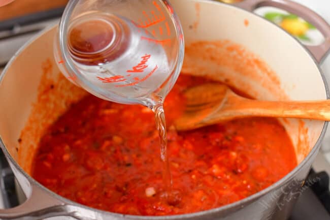 Vodka is being poured into a pot filled with a red tomato mixture.