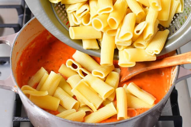 Cooked noodles are being poured into the pot full of sauce. 