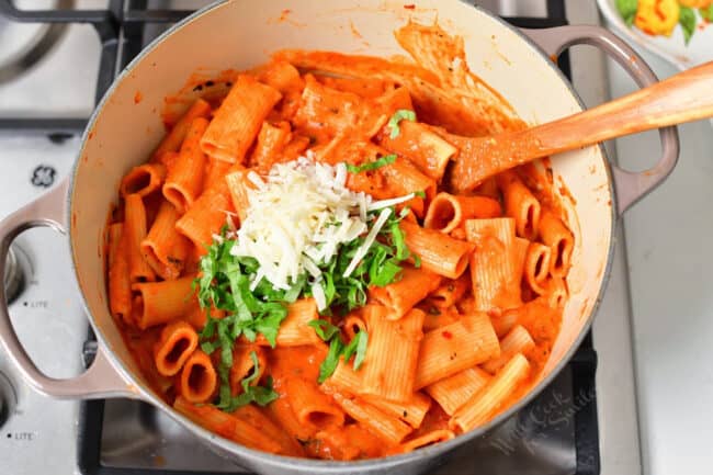 A pot is filled with basil and parmesan on top of coated noodles. 