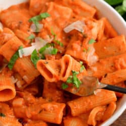 A fork is lifting a bite sized portion of pasta from a bowl.