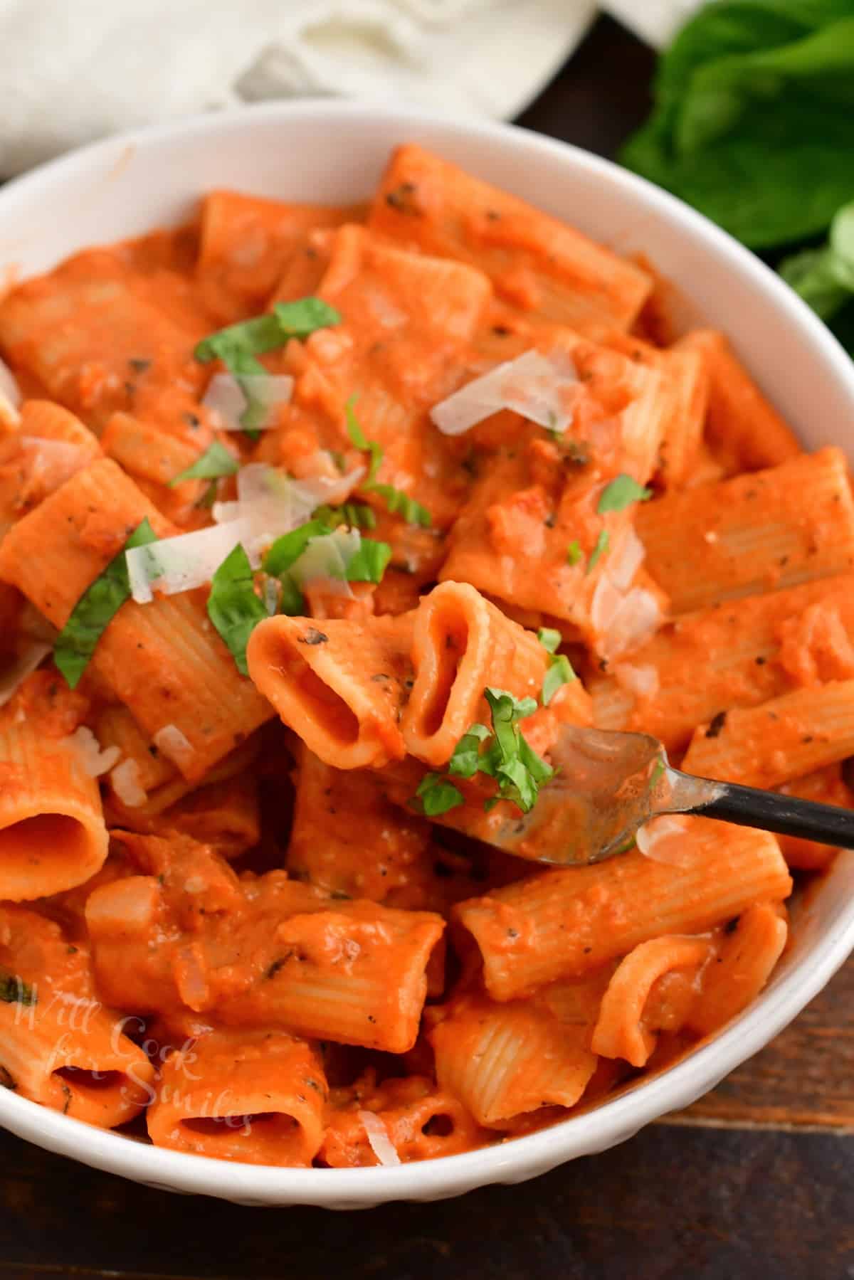 A fork is lifting a bite sized portion of pasta from a bowl. 