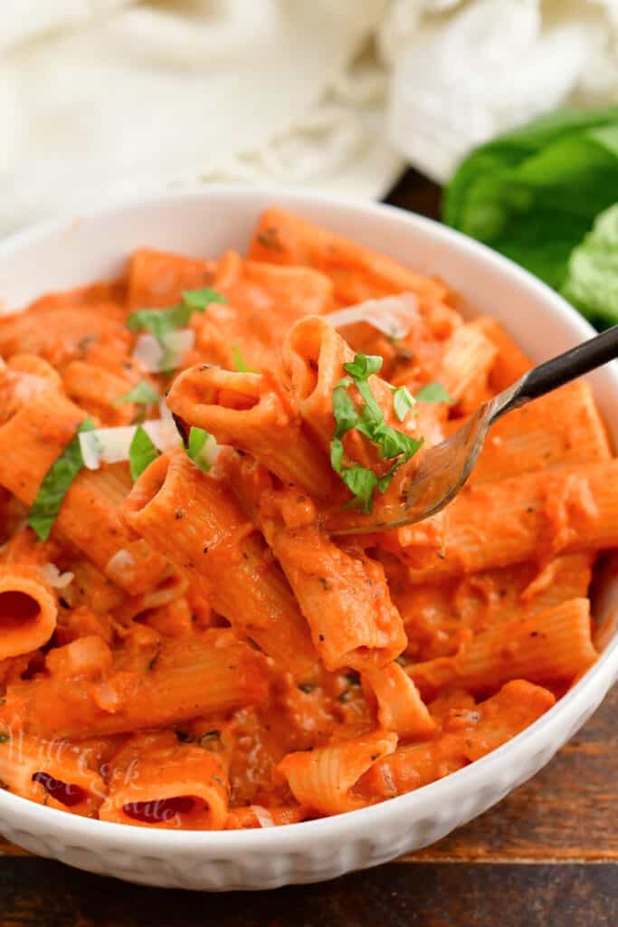 A fork is lifting a bite of penne alla vodka from the bowl. 